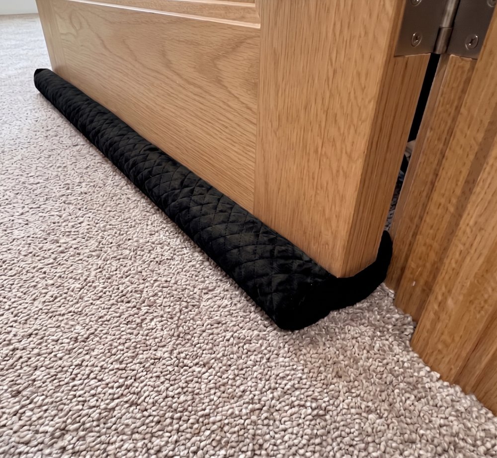 Twin Draft Guard Velvet in black quilted velvet under a wooden door on carpet